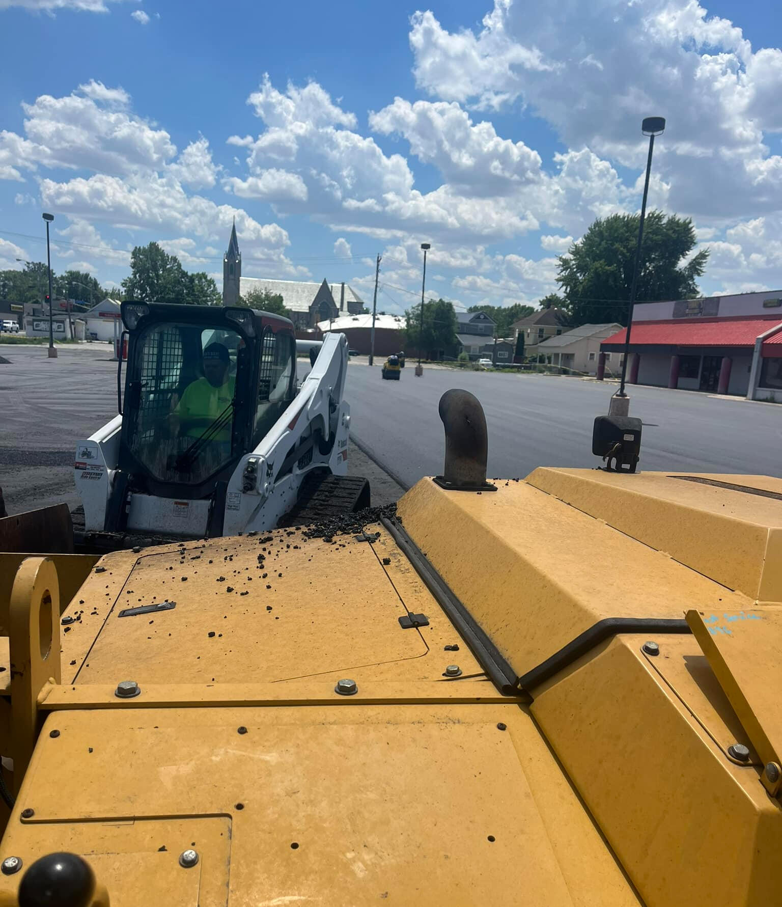 Industrial paving equipment laying asphalt with a Bobcat operator